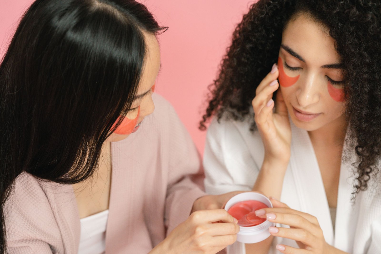Two women applying red eye patches in a skincare routine, focusing on beauty and self-care.