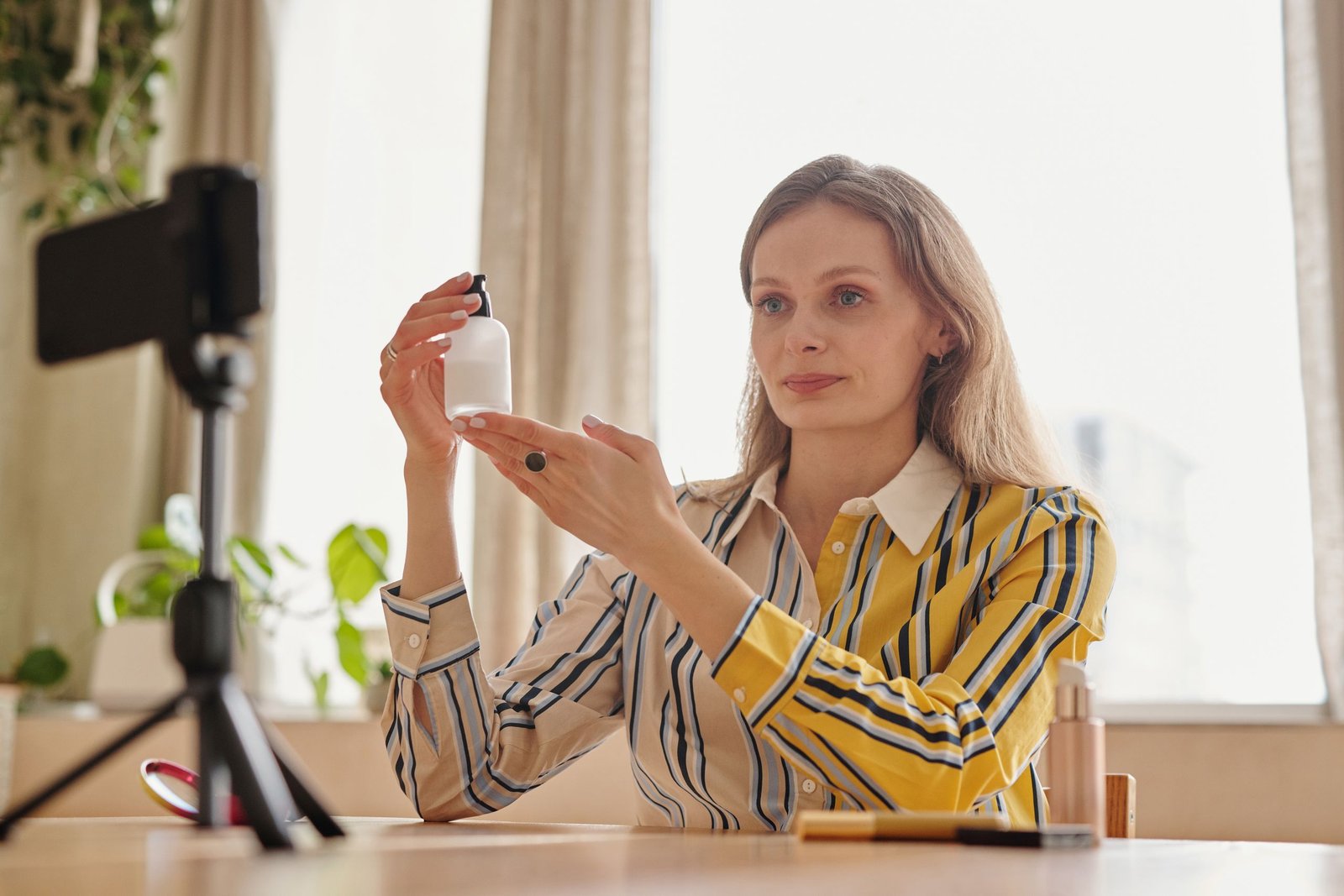 Woman demonstrates skincare product during a vlog in a cozy indoor setting.