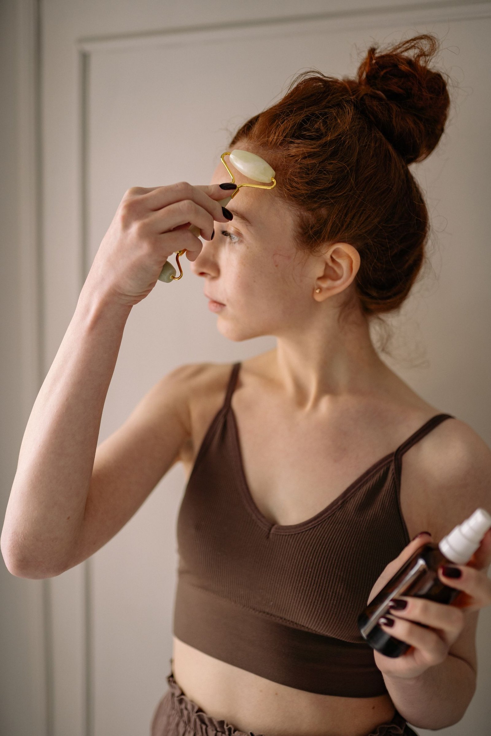 Young woman using a jade roller on her face as part of her morning skincare routine indoors.